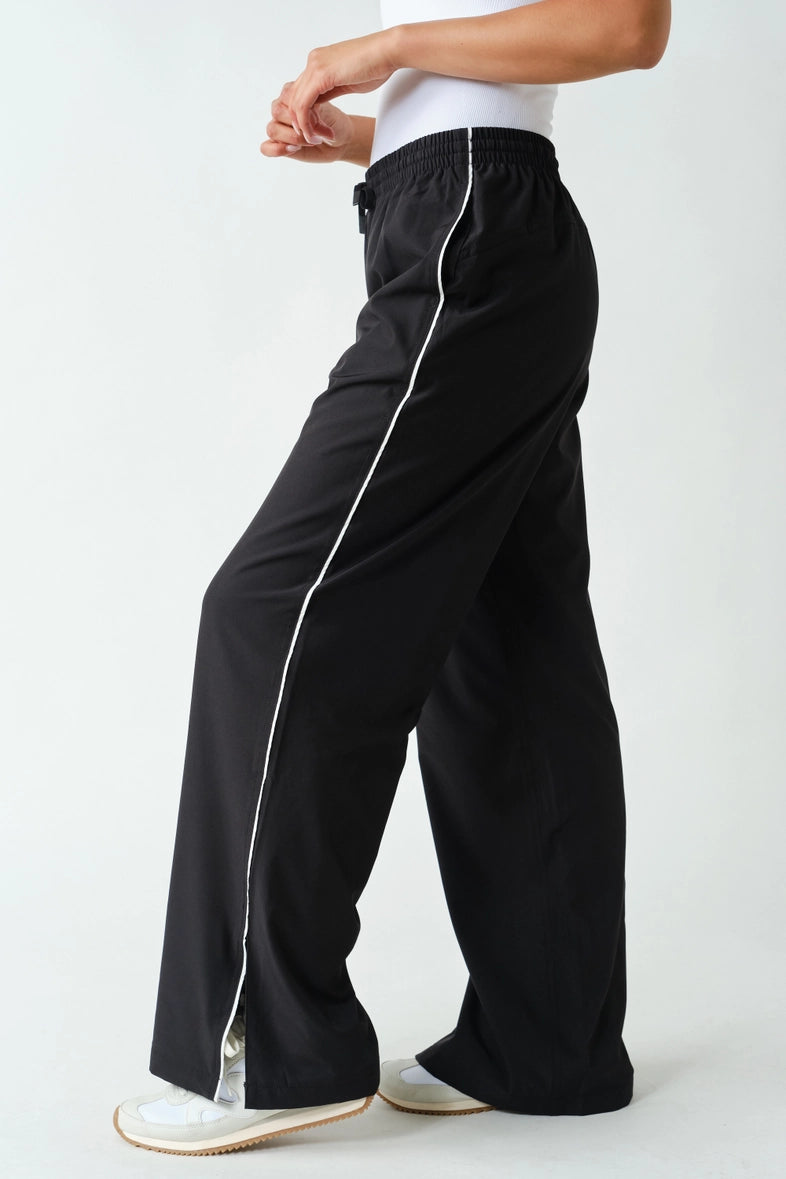 Black wide-leg track pants with white piping, side view